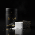 Black cylindrical container with gold "TITAN" logo next to a white chalk block on a reflective black surface.
