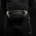 Black leather Titan Stealth fanny pack with gold zippers and raised gold logo, worn around the waist.